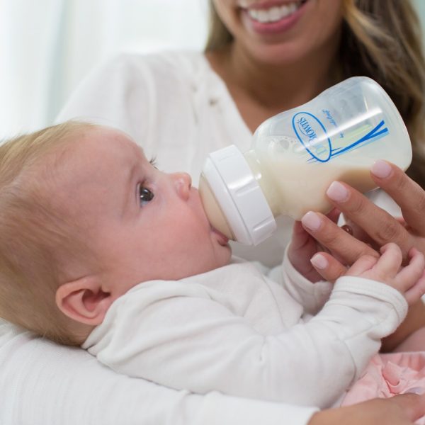 A mom holding a baby who is drinking from a Dr. Brown’s Natural Flow® Options+™ Anti-Colic Wide-Neck Bottle